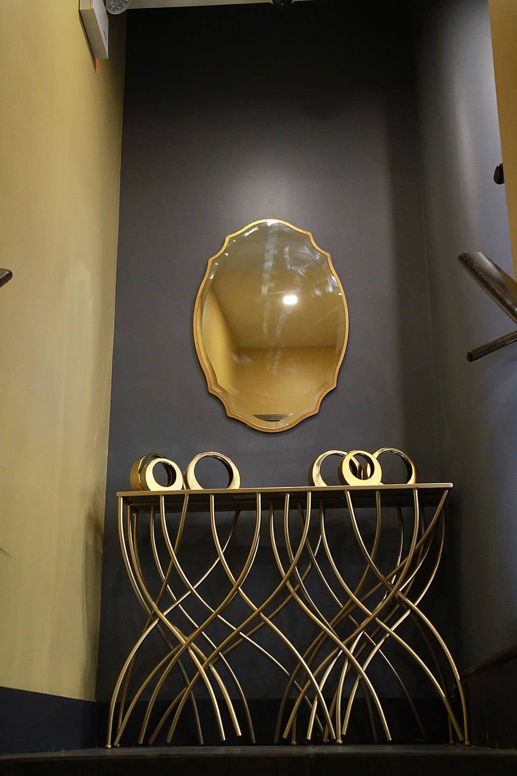 The image shows a decorative wall-mounted mirror within a room with dark walls and a patterned floor, reflecting the interior space.